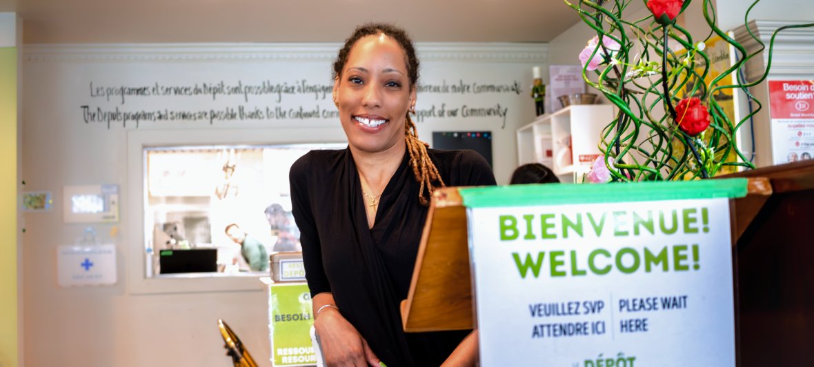 Une femme sourit devant un panneau d’accueil dans un centre communautaire d’alimentation.